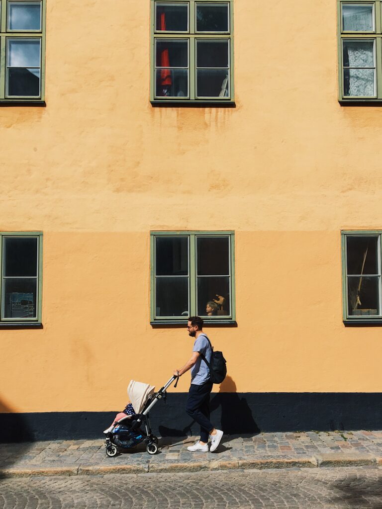 Daddy walking his baby in a stroller in front of one of Stockholm's emblematic creamy façades in Södermalm.
