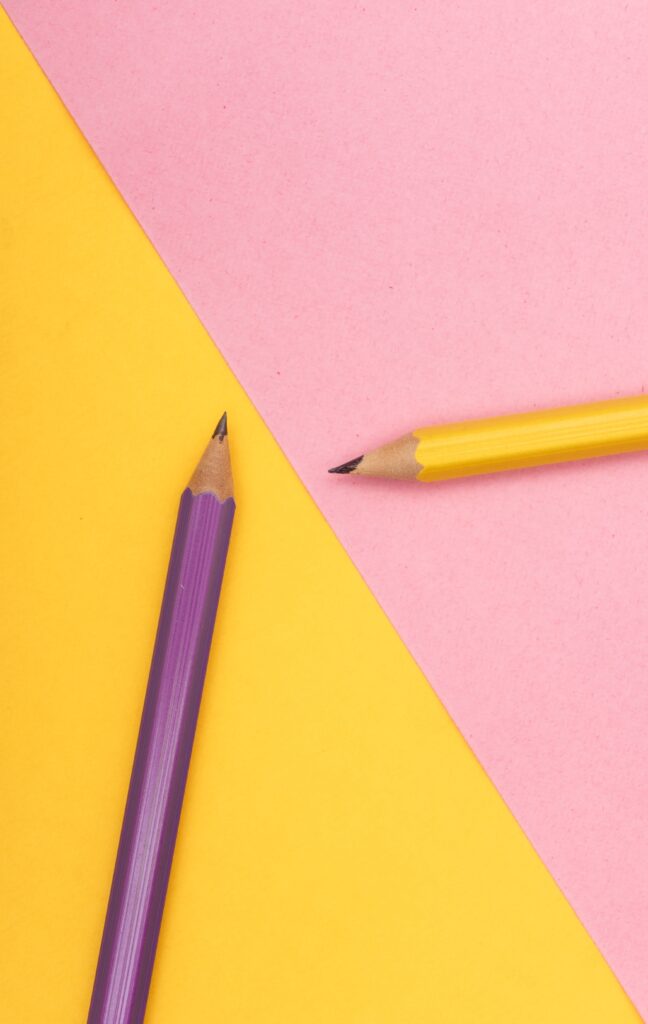 A purple pencil and yellow pencil on pink and yellow paper.