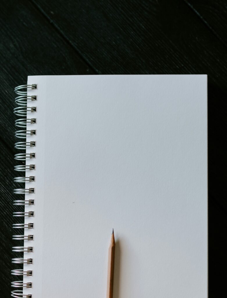 A sharpened pencil sits on top of a blank spiral notebook.