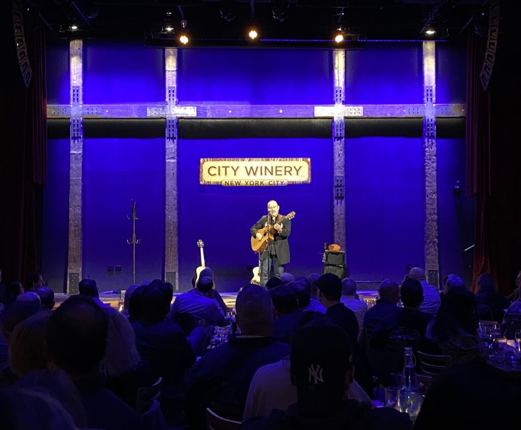 Colin Hay plays guitar in front of a crowd at New York's City Winery.