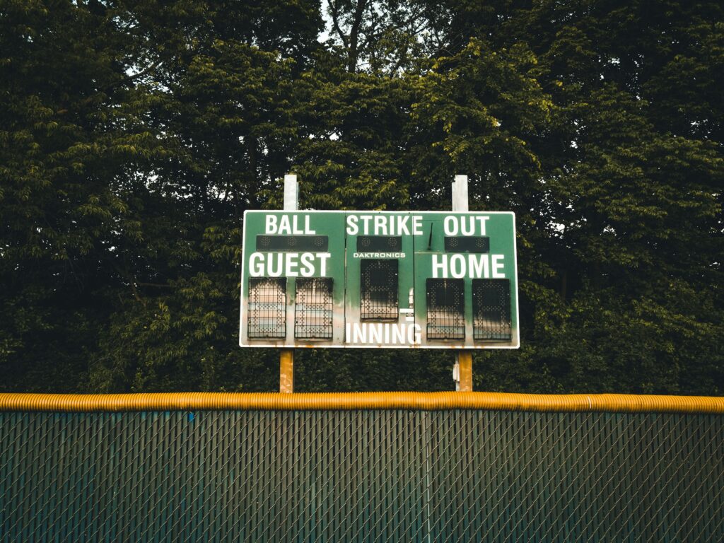 A green scoreboard sits beyond an outfield fence at a baseball stadium.