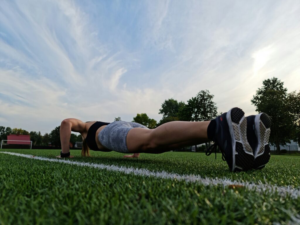 A woman does a push-up on a green soccer field.